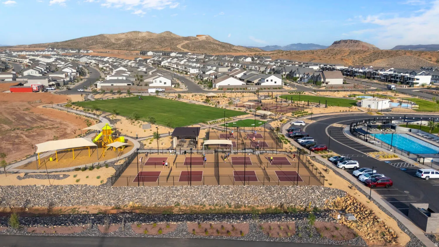 Community recreation area featuring multiple pickleball courts, a playground with shade structures, and an expansive aquatic facility with a swimming pool