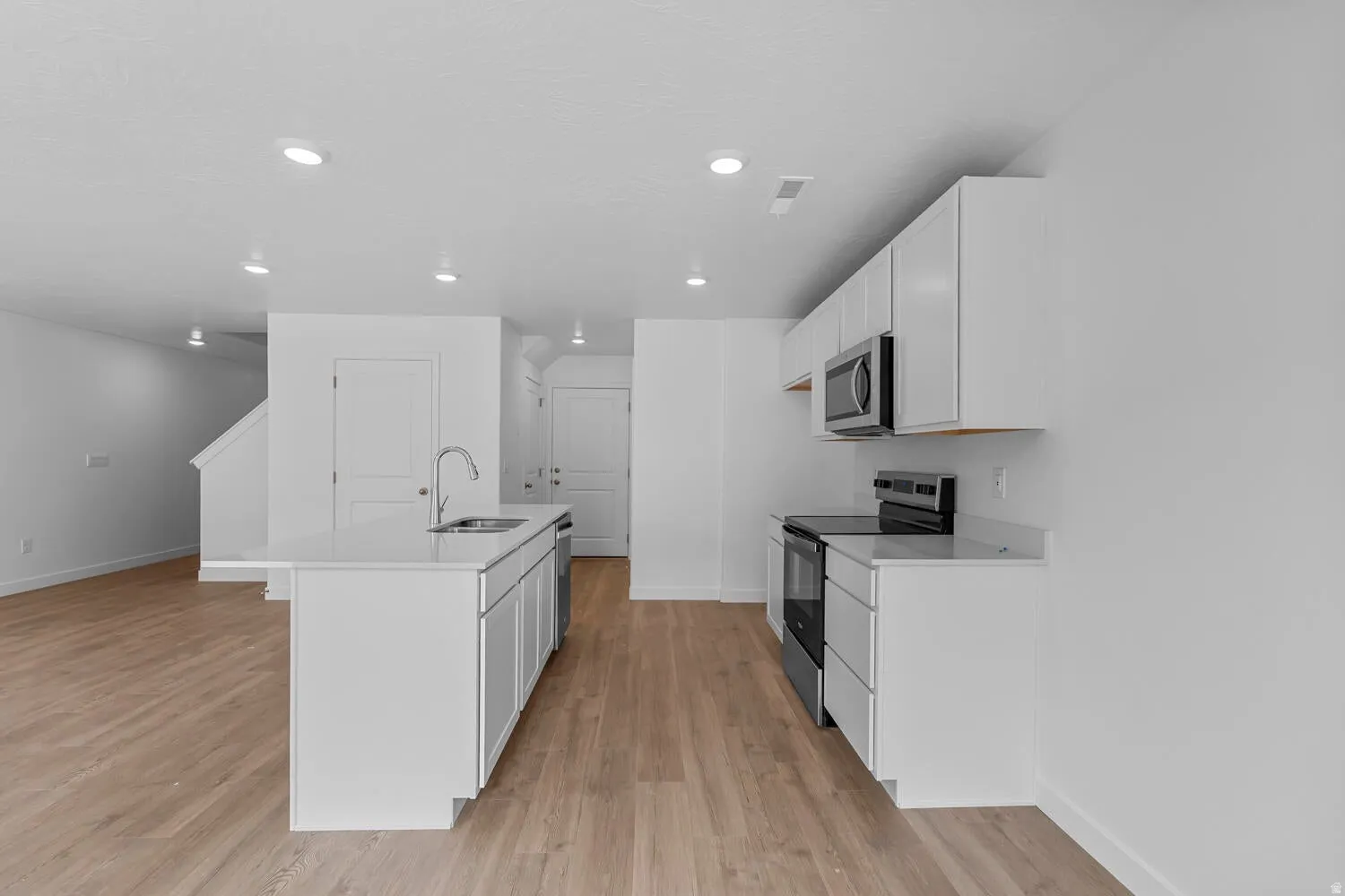 Modern kitchen featuring an island with a stainless steel sink, white cabinetry, a built-in microwave, and wood-finish flooring throughout