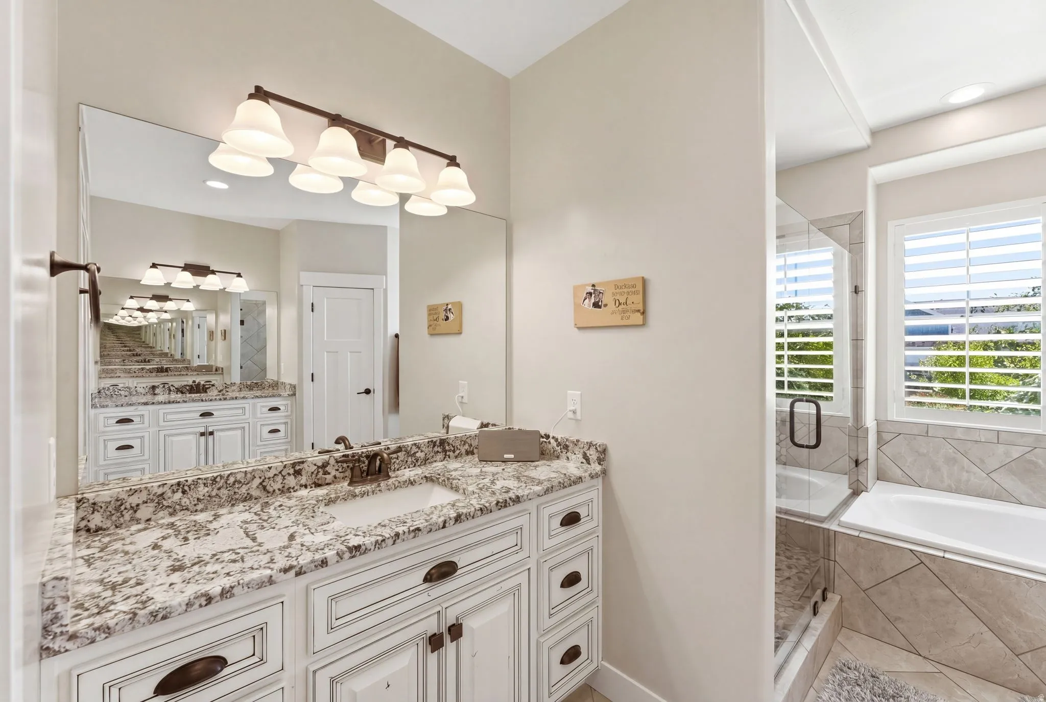 Bathroom featuring a double vanity with stone countertops, a full-width mirror, and a bronze six-light fixture