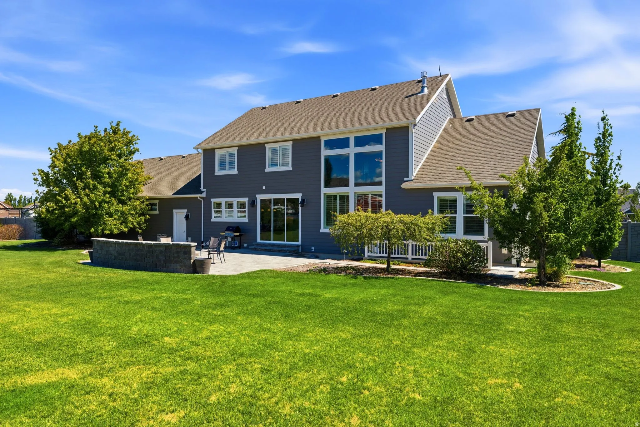 Expansive rear elevation featuring blue siding, a stone-accented patio, and a retaining wall