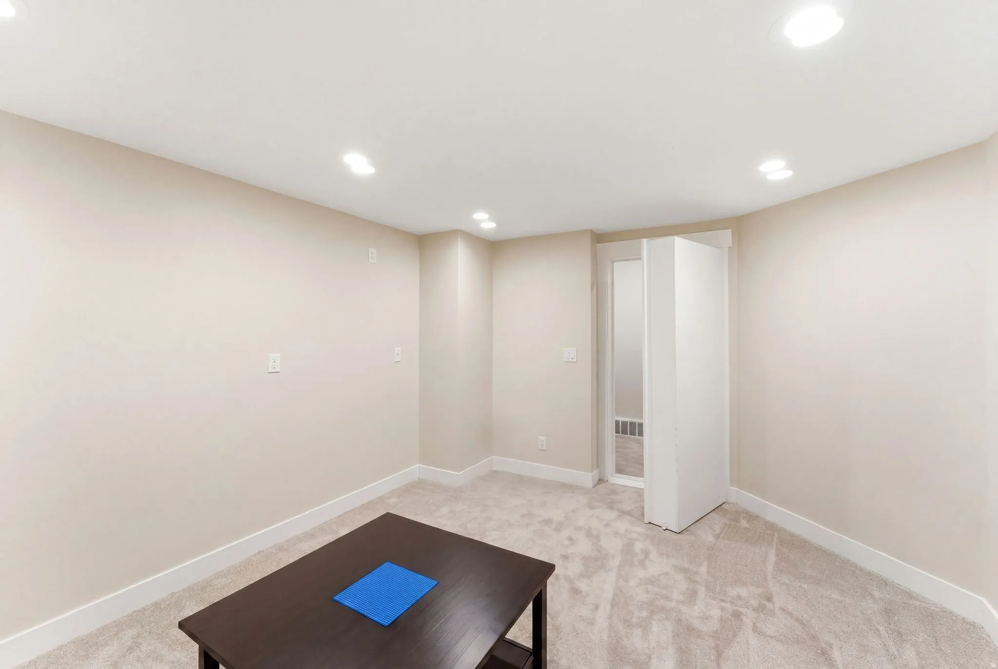 Carpeted room featuring recessed lighting, light-toned walls, white baseboards, and a framed doorway opening