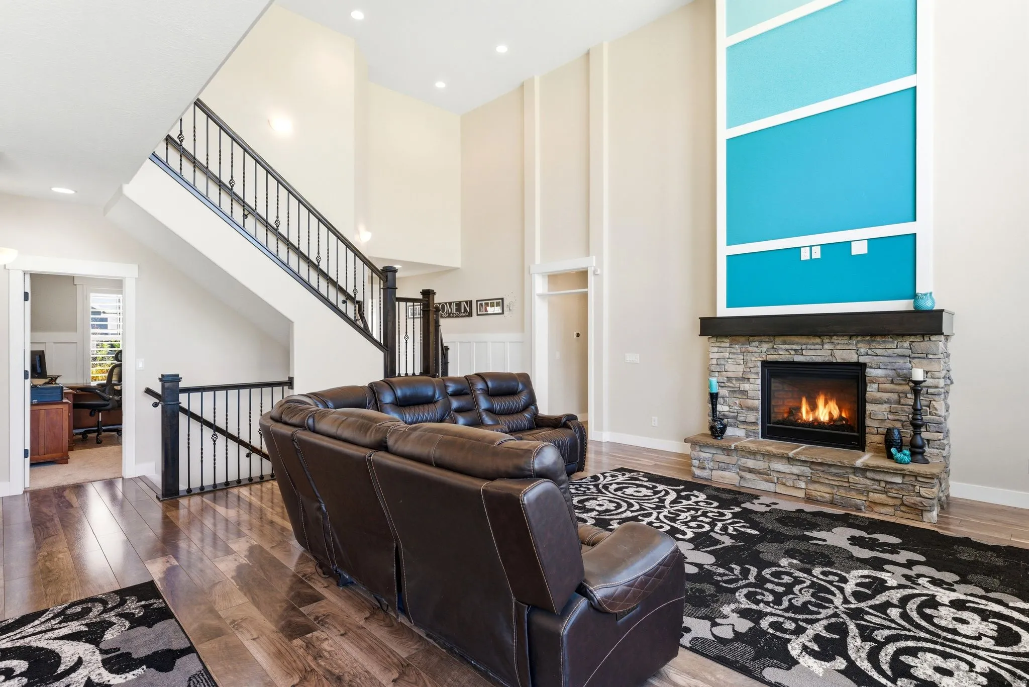 Two-story living area featuring a stacked stone fireplace with a dark wood mantel, high ceilings with recessed lighting, and wood-finish flooring