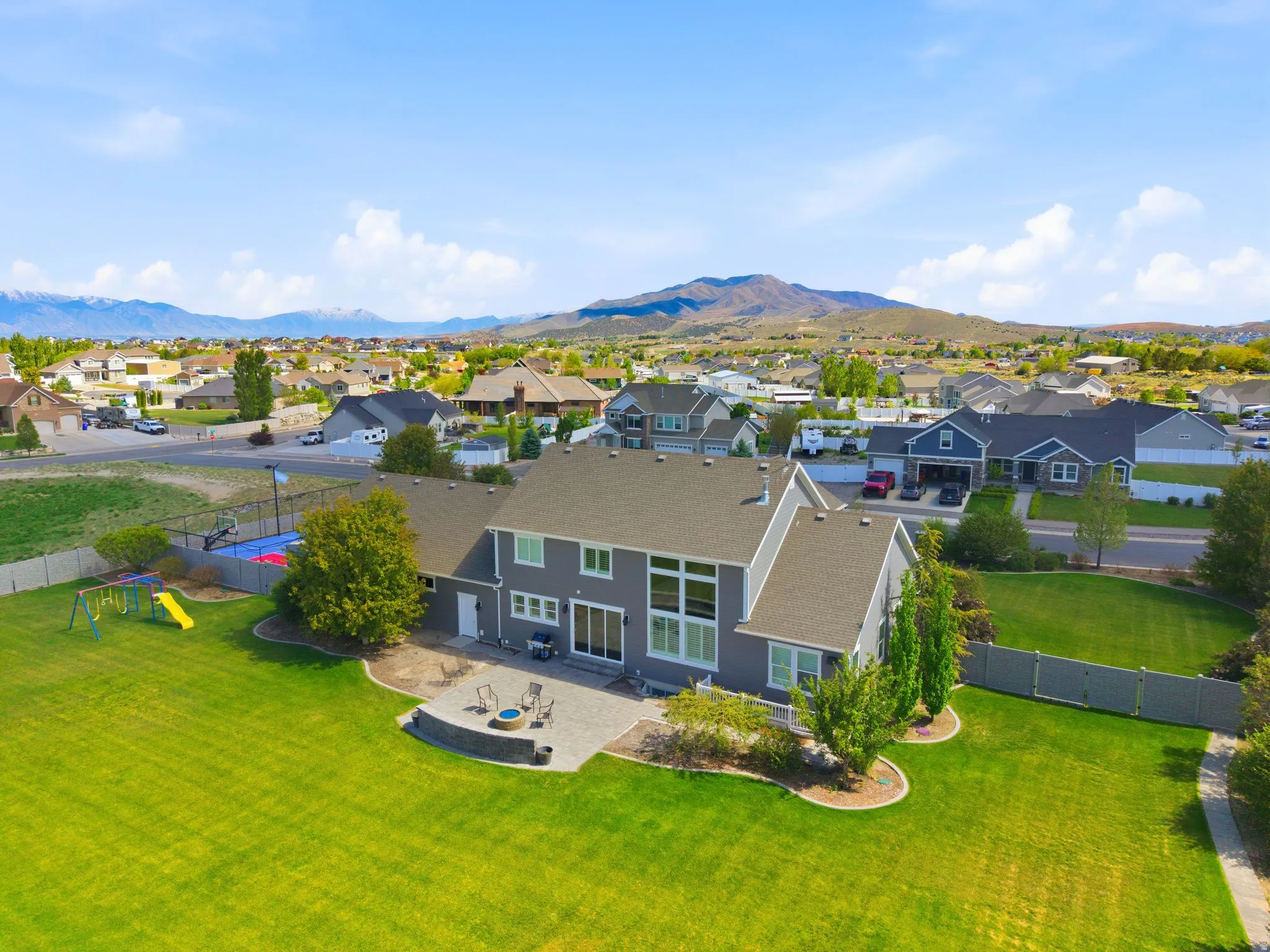 Expansive rear yard featuring a manicured lawn, a large paver patio with a built-in fire pit, and a multi-sport court