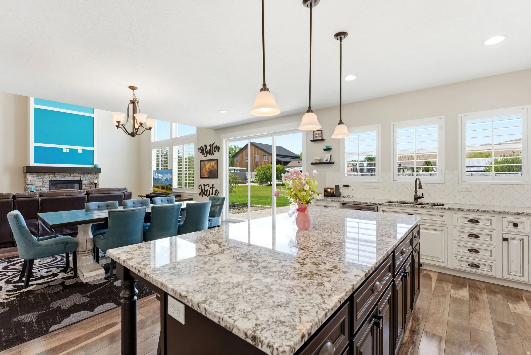 Contemporary kitchen featuring a granite-topped island with pendant lighting, white cabinetry, herringbone tile backsplash, and wood-finish flooring