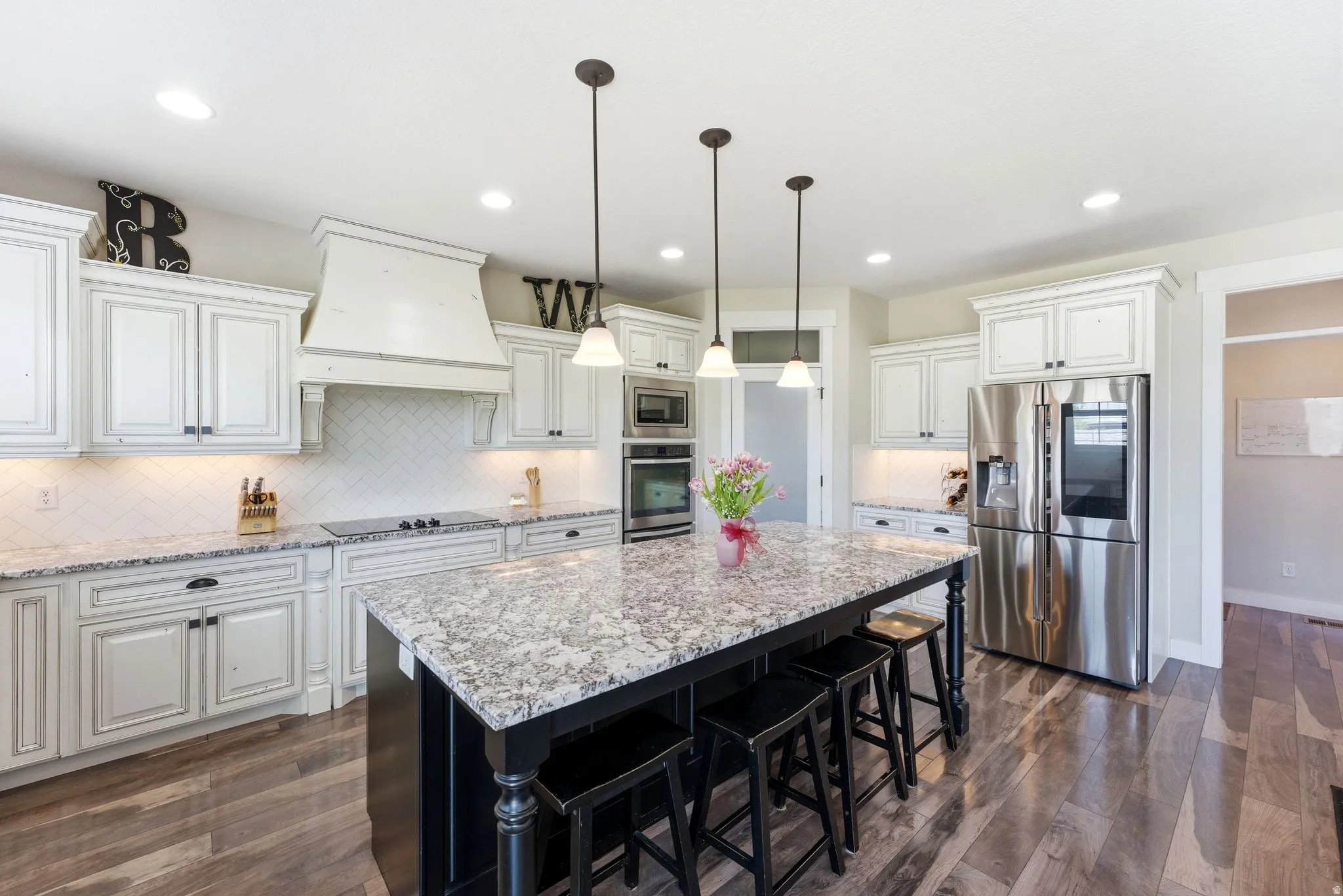 Kitchen featuring a large central island with seating, pendant lighting, stainless steel appliances, wood-finish flooring, and white cabinetry with dark hardware