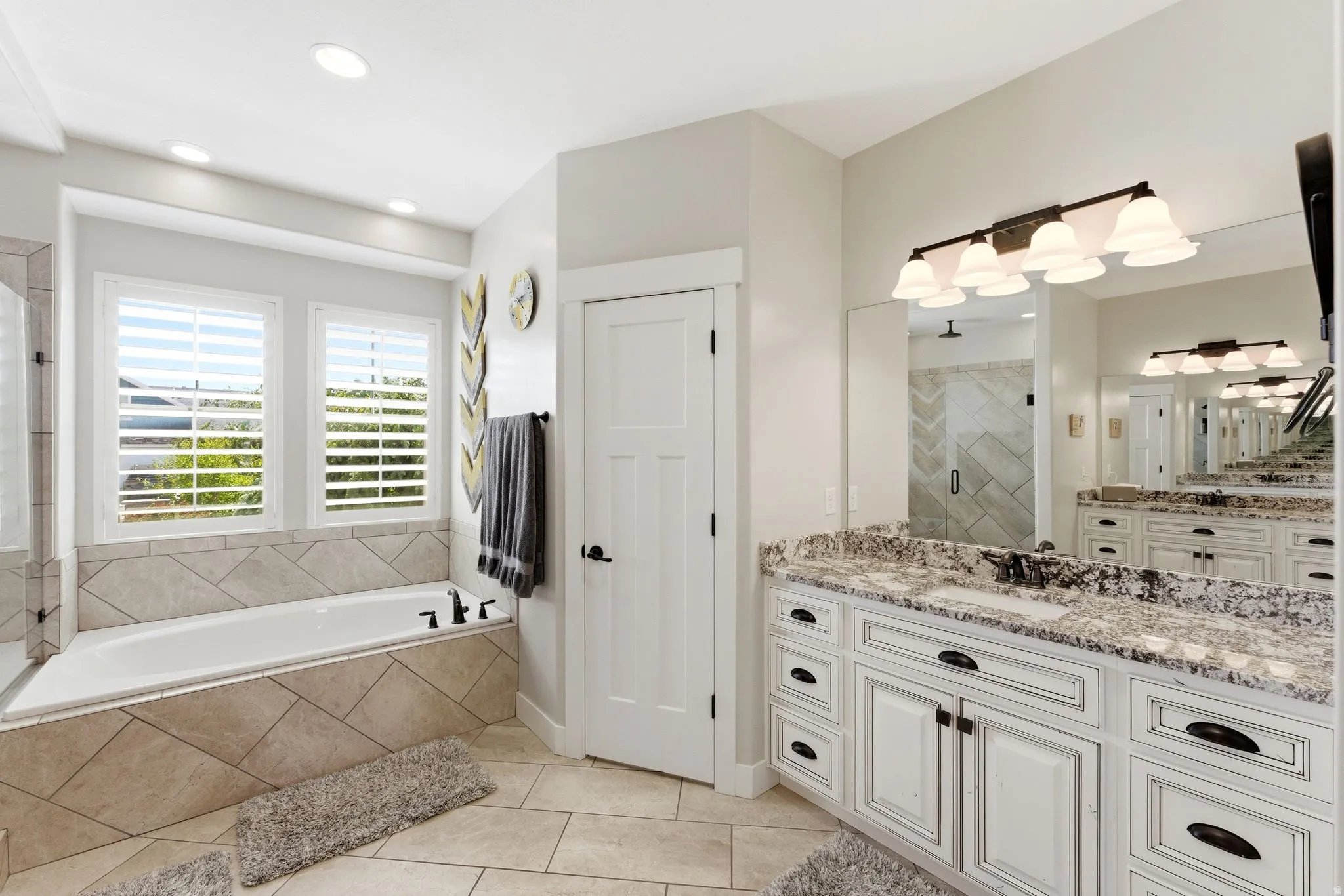 Spacious bathroom featuring a dual vanity with granite countertops, an undermount sink, and white cabinetry