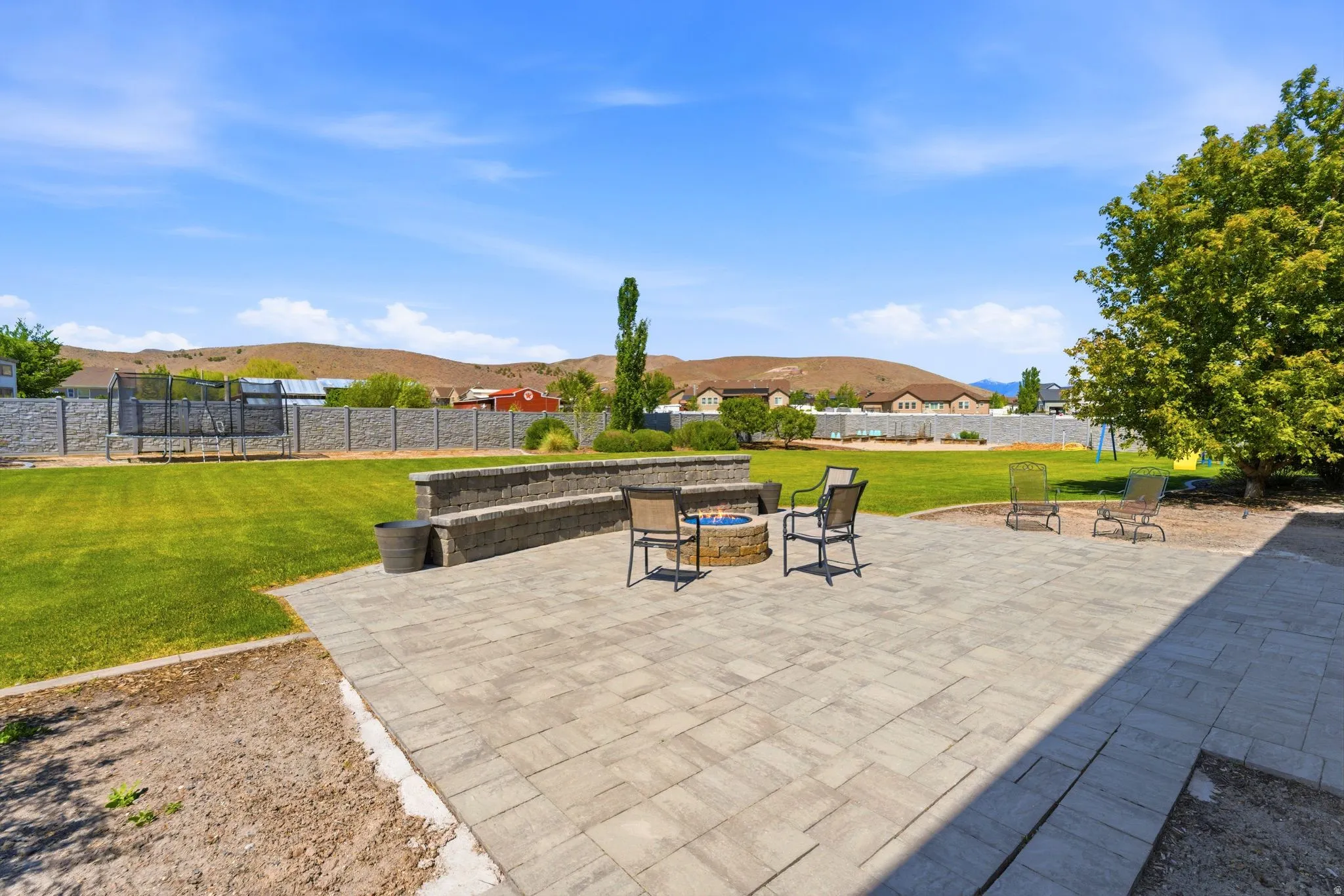 Expansive paver patio featuring a built-in fire pit, stone-clad seating wall, and generous green space