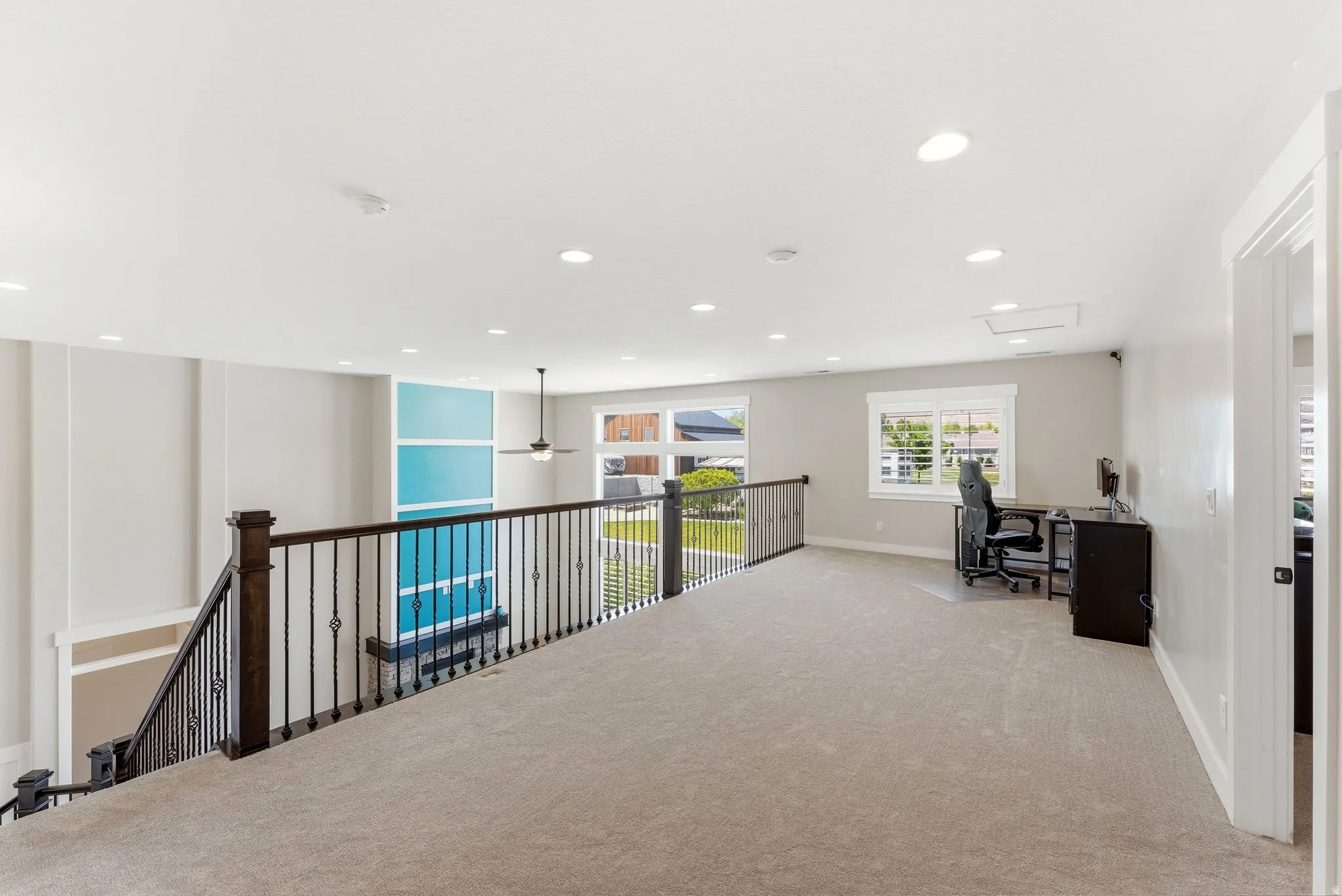 Expansive loft area featuring neutral carpeting, recessed lighting, and a dark wood and wrought iron railing