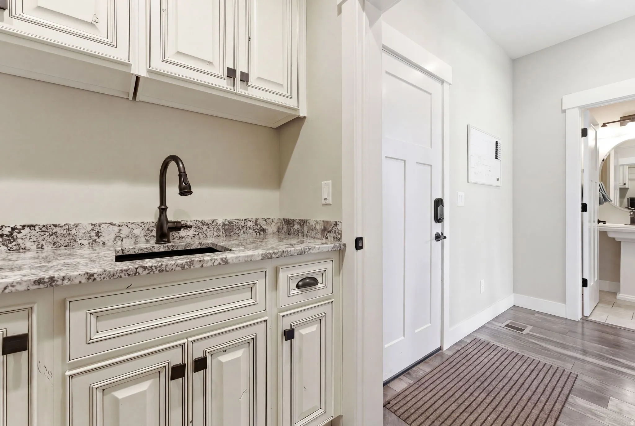 Utility sink with a dark bronze faucet, stone countertop, white shaker-style cabinetry, and wood-finish flooring