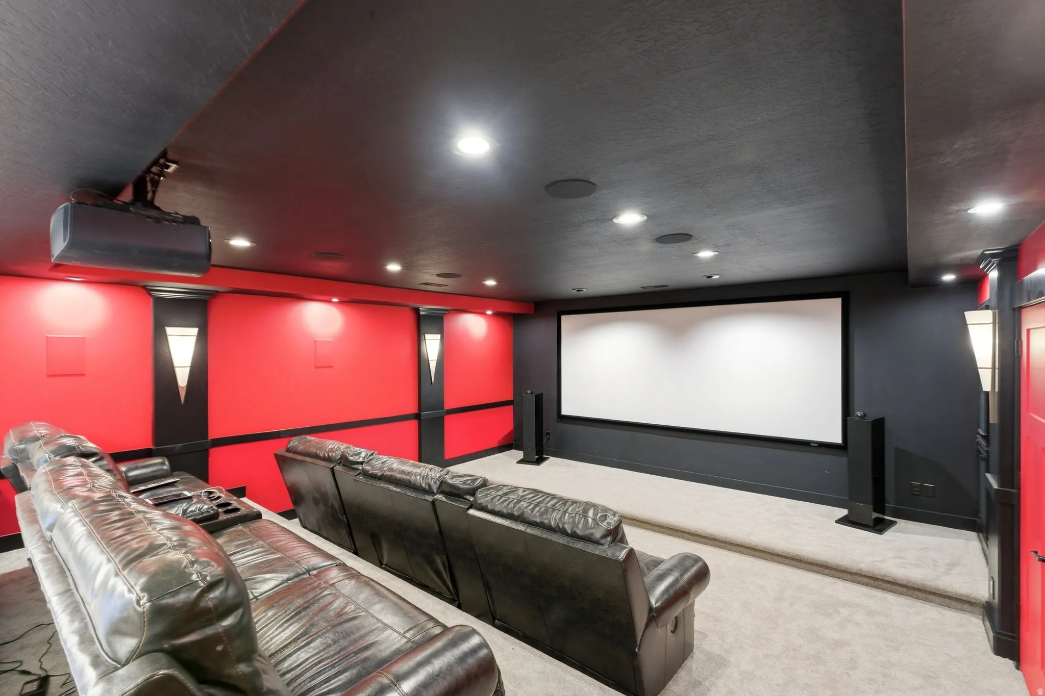 Dedicated media room featuring a large projection screen, recessed ceiling lighting, and a tiered viewing area with carpeting