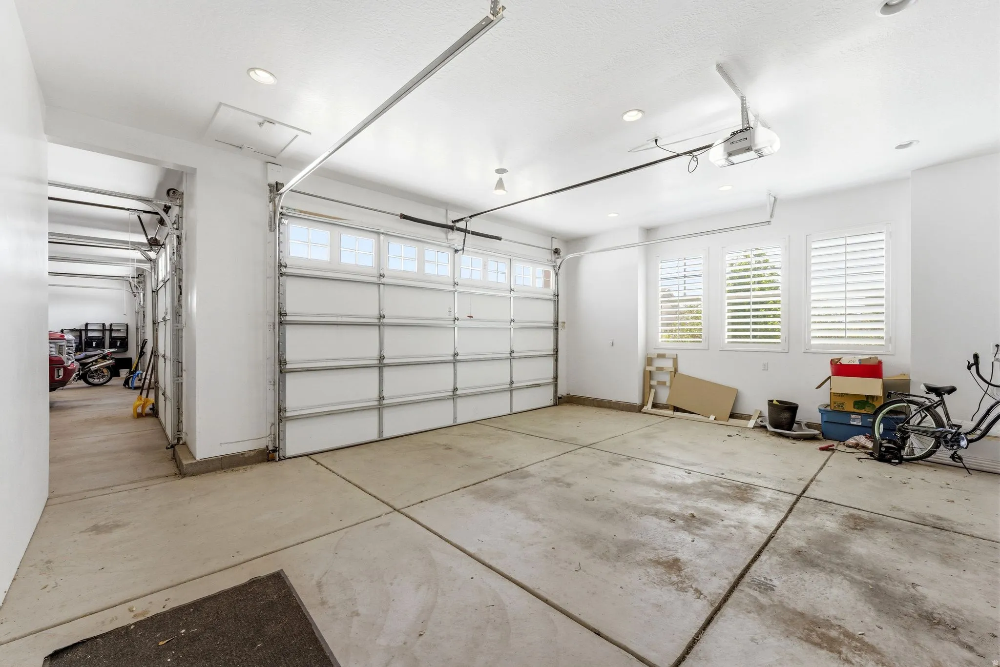 Spacious garage featuring a sectional garage door with upper window panels, multiple recessed ceiling lights, and three windows with louvered shutters