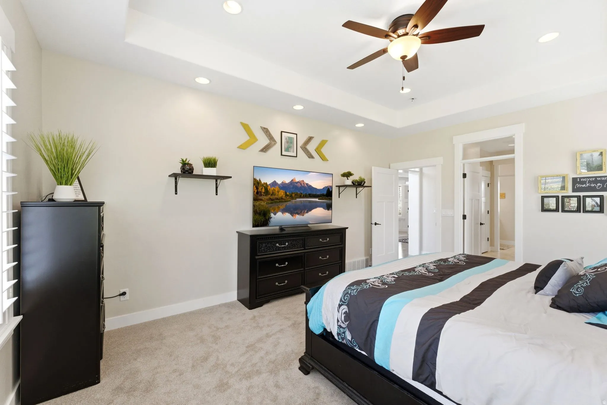 Recessed lighting illuminates the tray ceiling in this carpeted room, featuring white baseboards and trim, and a ceiling fan