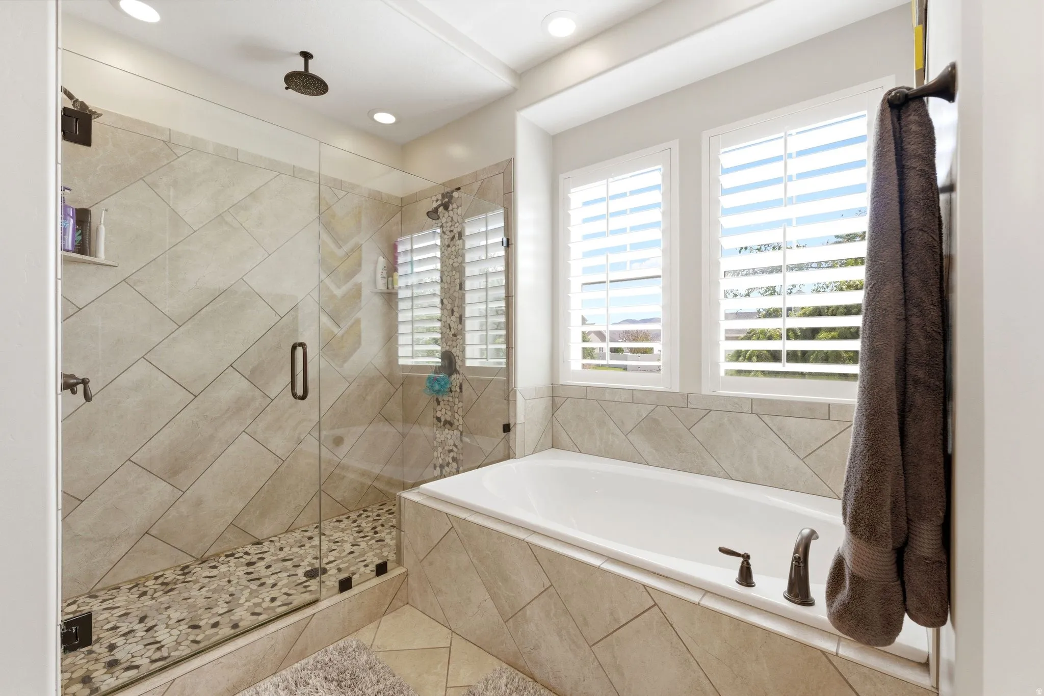 Spacious bathroom featuring a built-in soaking tub, glass-enclosed shower with pebbled floor, ceiling-mounted shower head, and tile surround