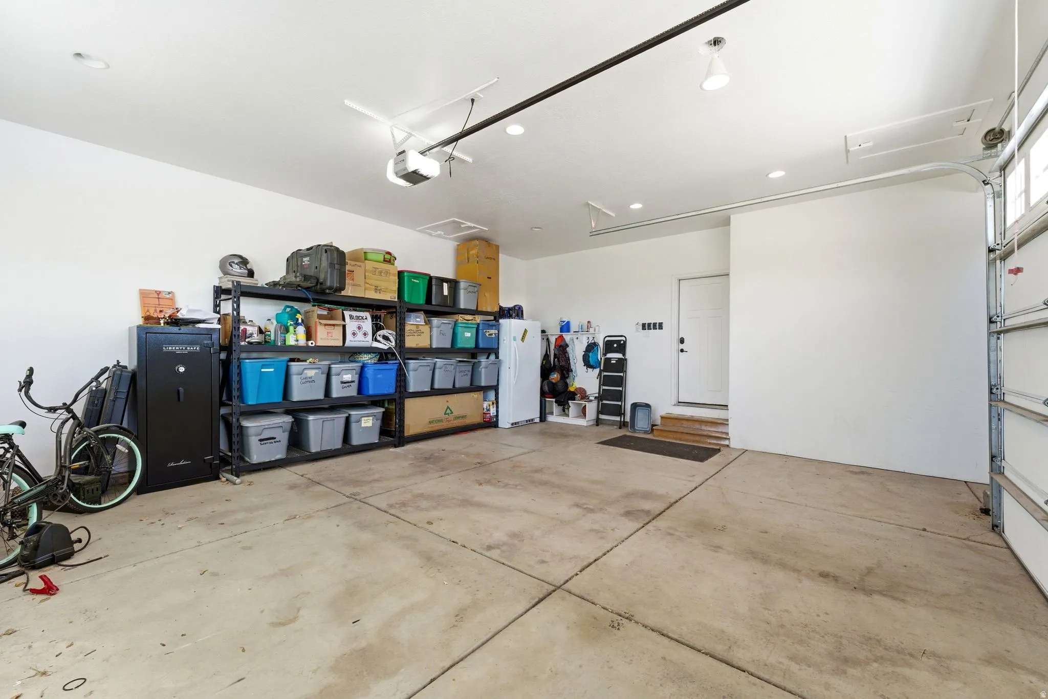 Spacious garage featuring a concrete floor, white walls, overhead lighting, and an overhead garage door