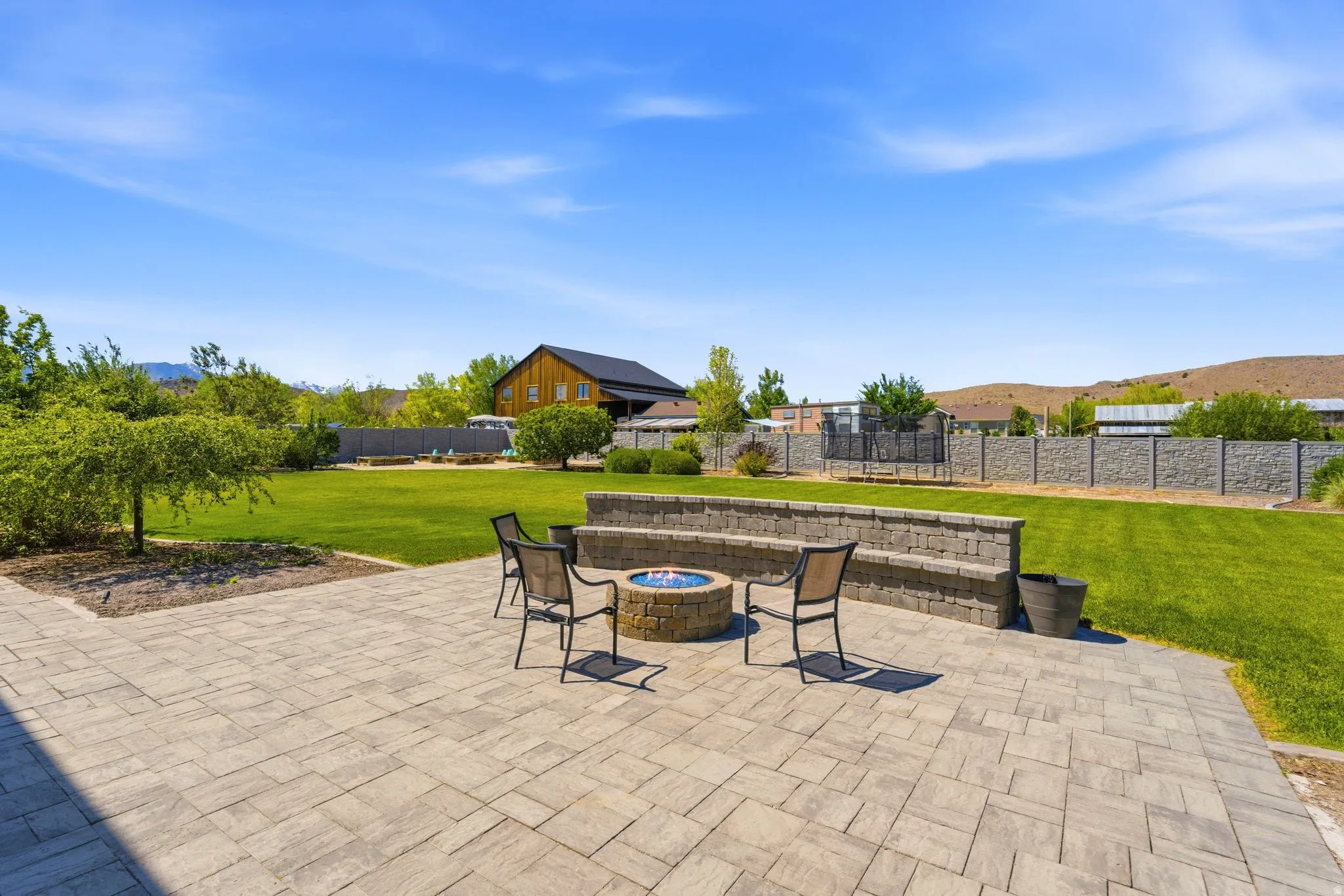 Expansive paved patio featuring a built-in stone fire pit and a tiered stone retaining wall