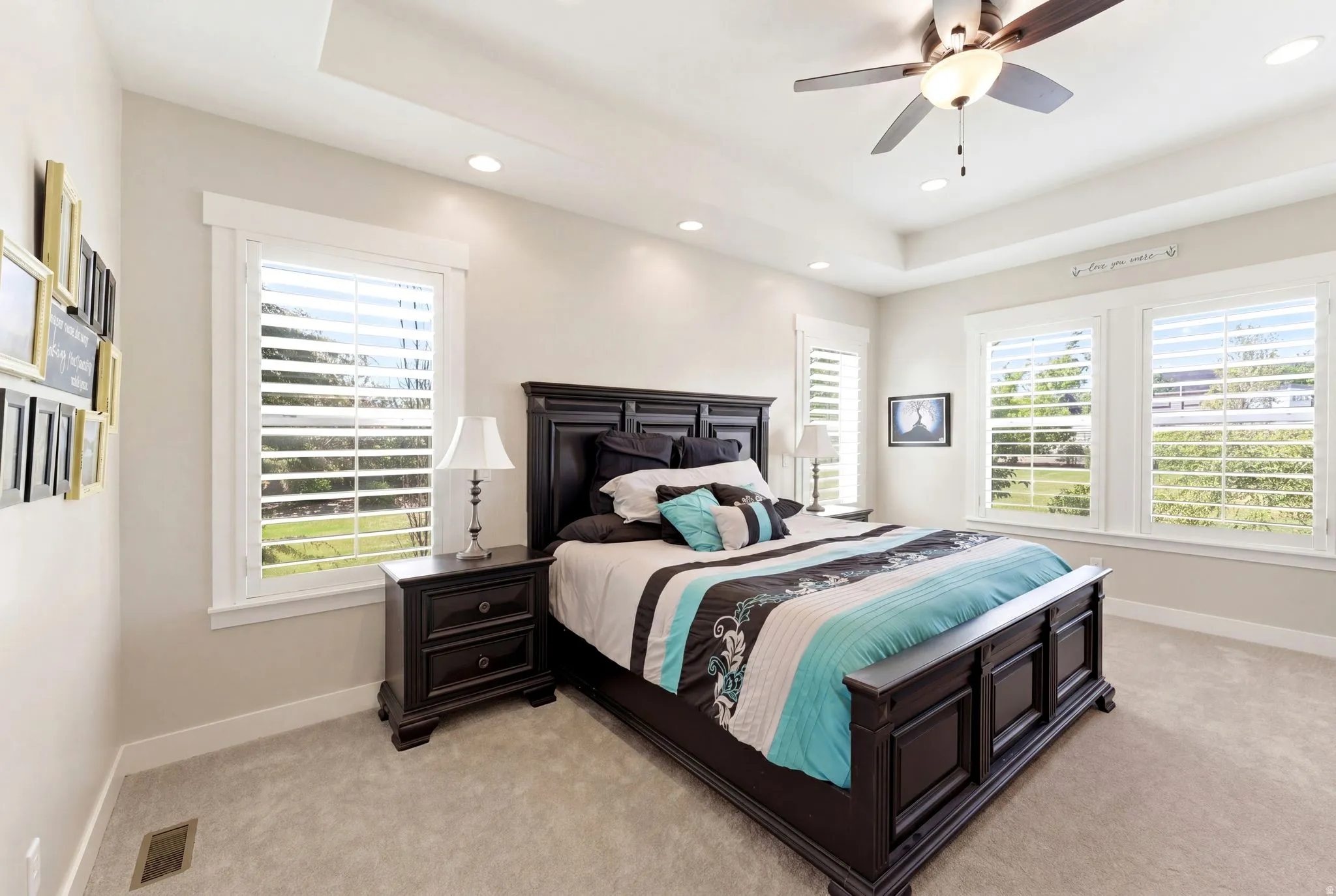 Tray ceiling with recessed lighting and a ceiling fan, featuring multiple windows with plantation shutters, light-toned wall paint, white trim, and light-toned carpeting