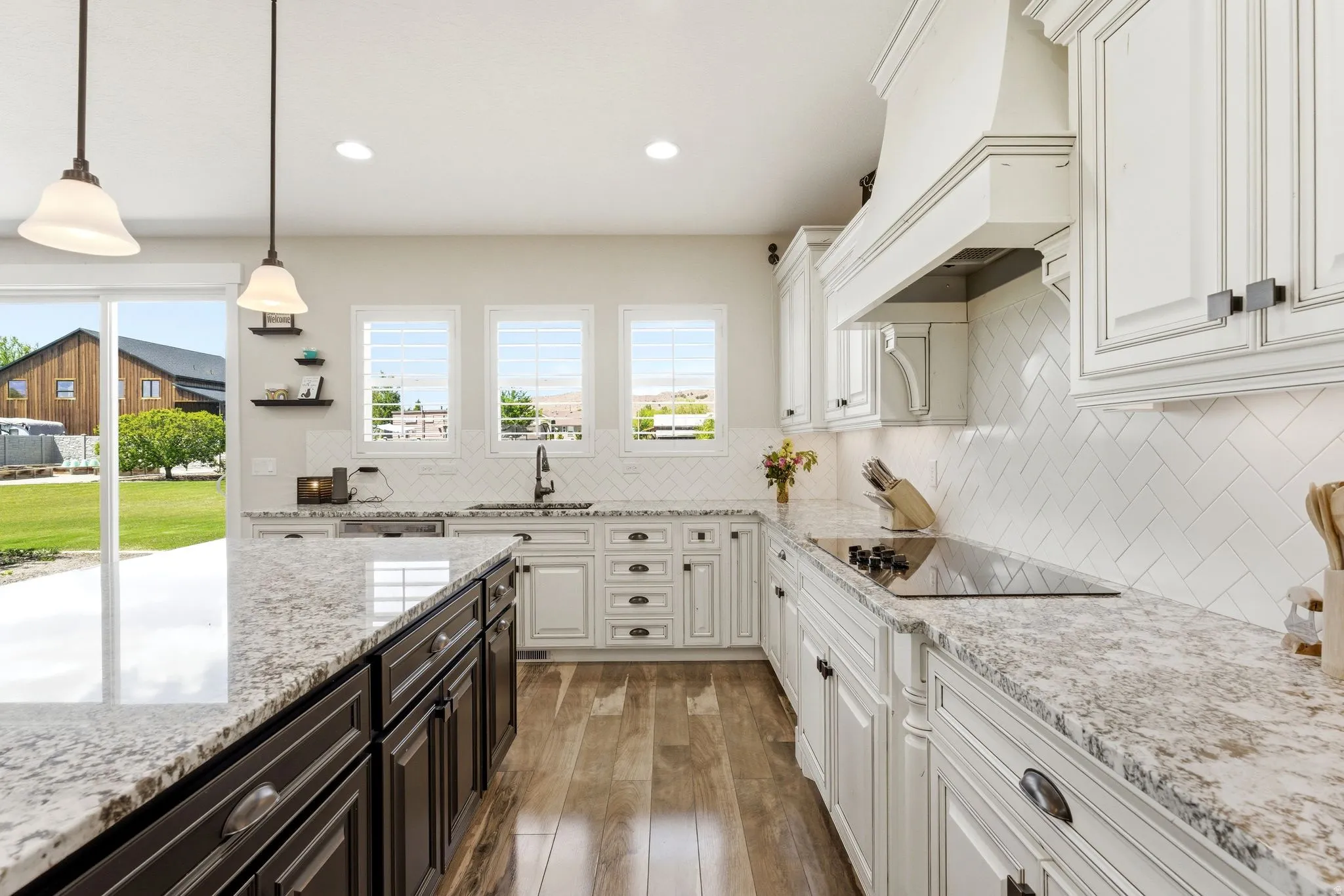 Gourmet kitchen featuring a central island with integrated storage, light-toned countertops, a smooth cooktop, and herringbone tile backsplash
