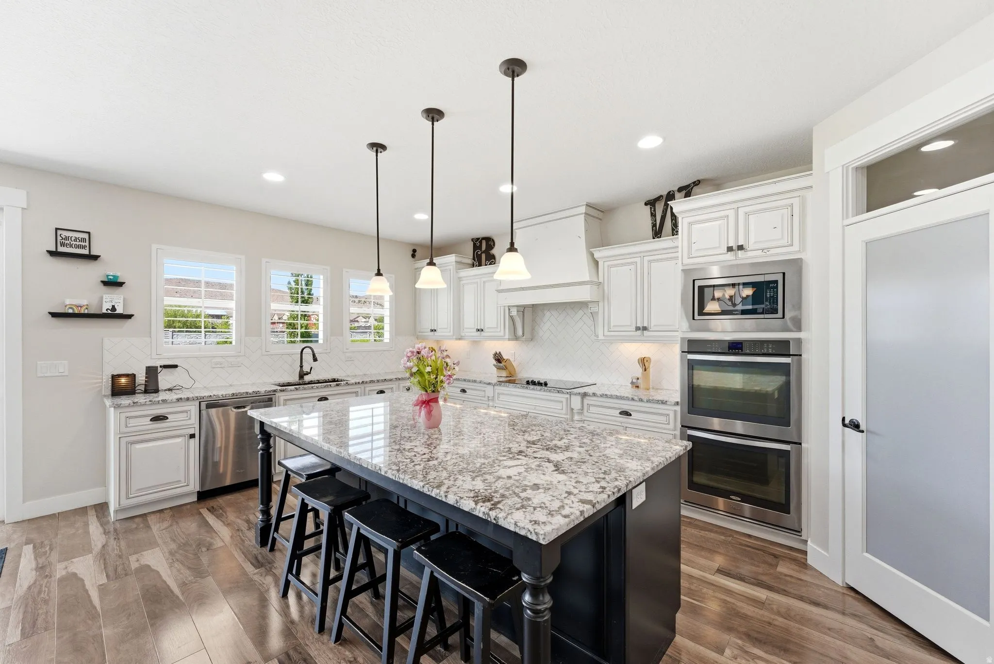 Spacious kitchen featuring an expansive center island with seating, pendant lighting, stainless steel appliances, and wood-finish flooring