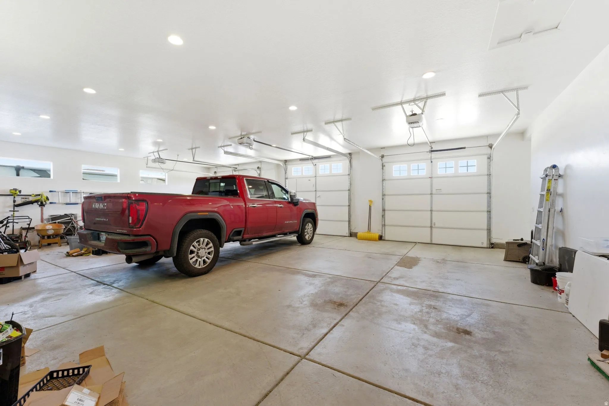 Spacious garage featuring a concrete floor, two white overhead doors with frosted window panels, recessed lighting, and horizontal transom windows