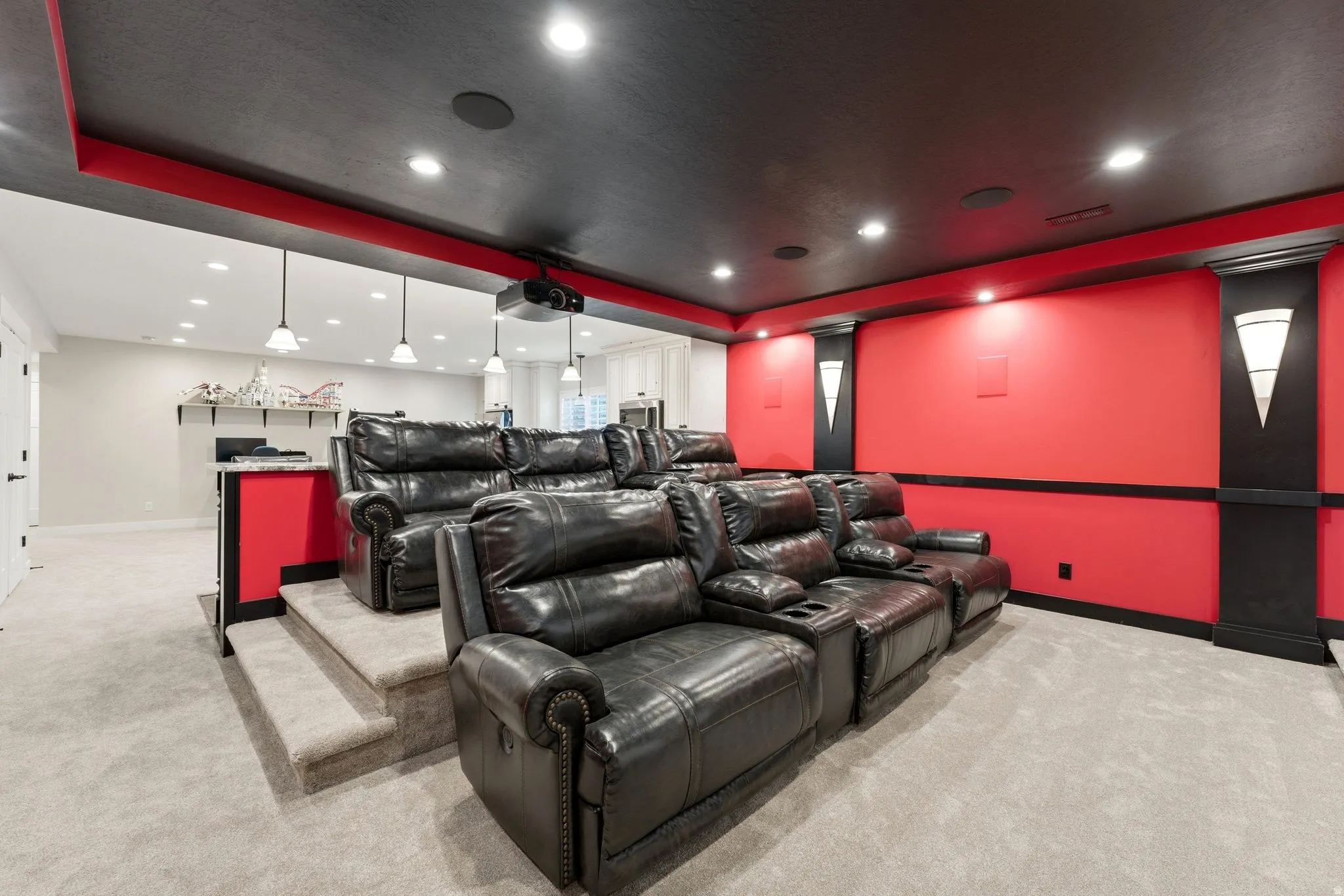Dedicated media room featuring tiered seating, recessed lighting, red accent walls, and a projection system
