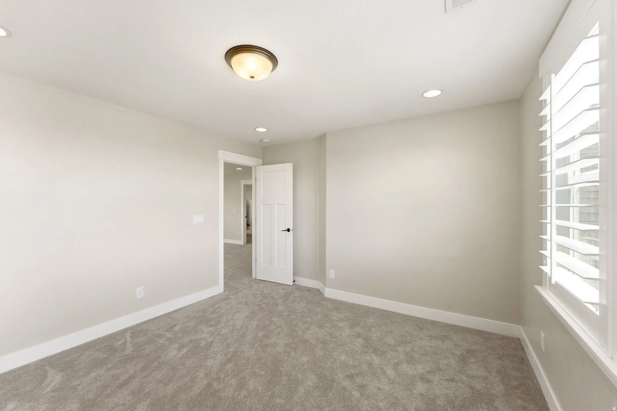 Carpeted room featuring a white paneled door, recessed lighting, and a window with plantation shutters