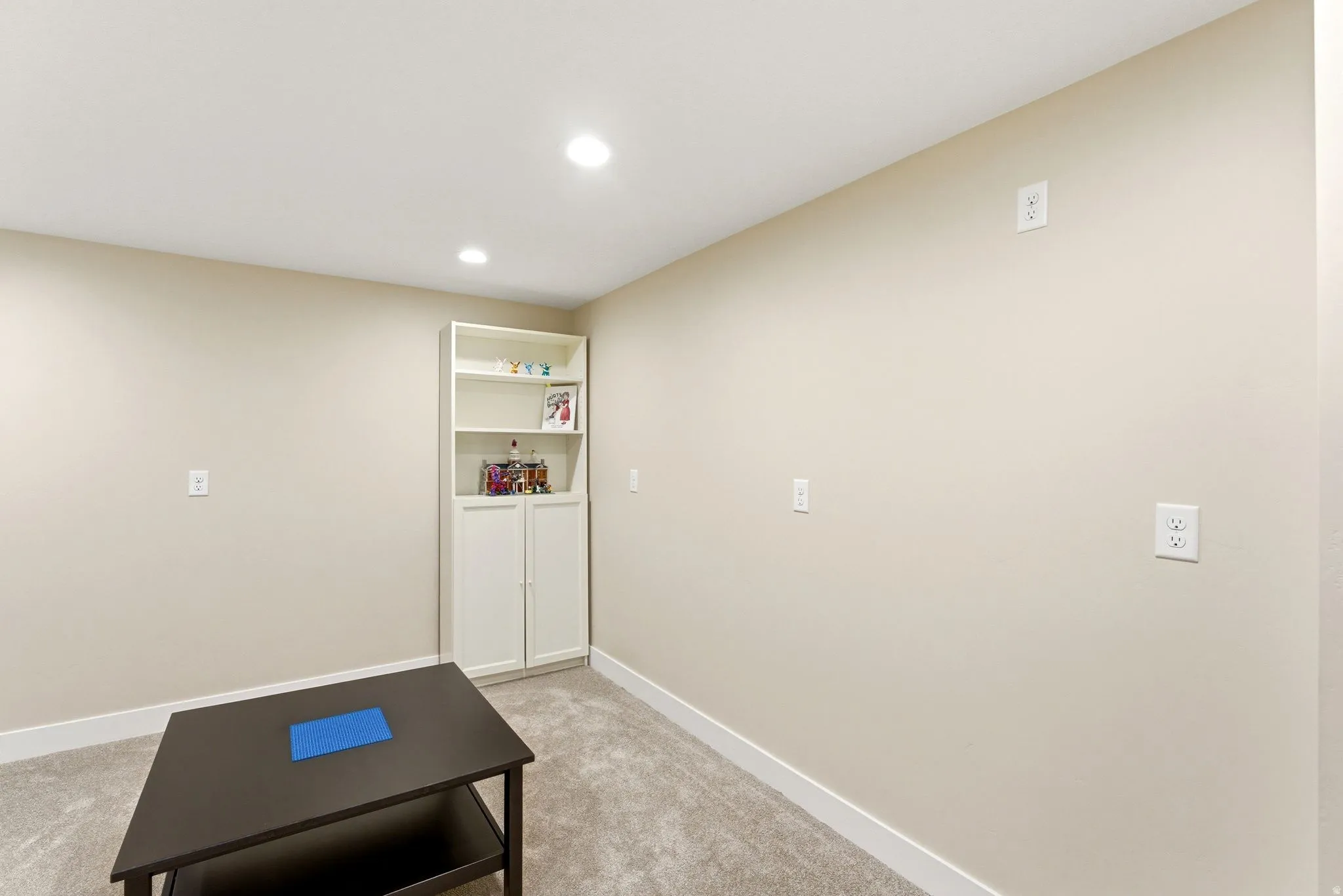 Recessed lighting illuminates a neutral painted room featuring a built-in white shelving unit with cabinet storage
