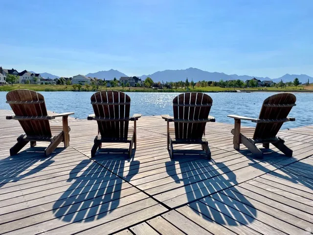 Expansive wooden dock with four Adirondack chairs overlooking a tranquil body of water