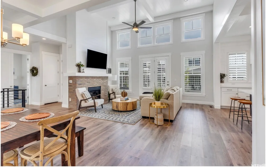 Spacious living area featuring a two-story ceiling, wood-finish flooring, a stone-clad fireplace, and multiple tall windows with plantation shutters