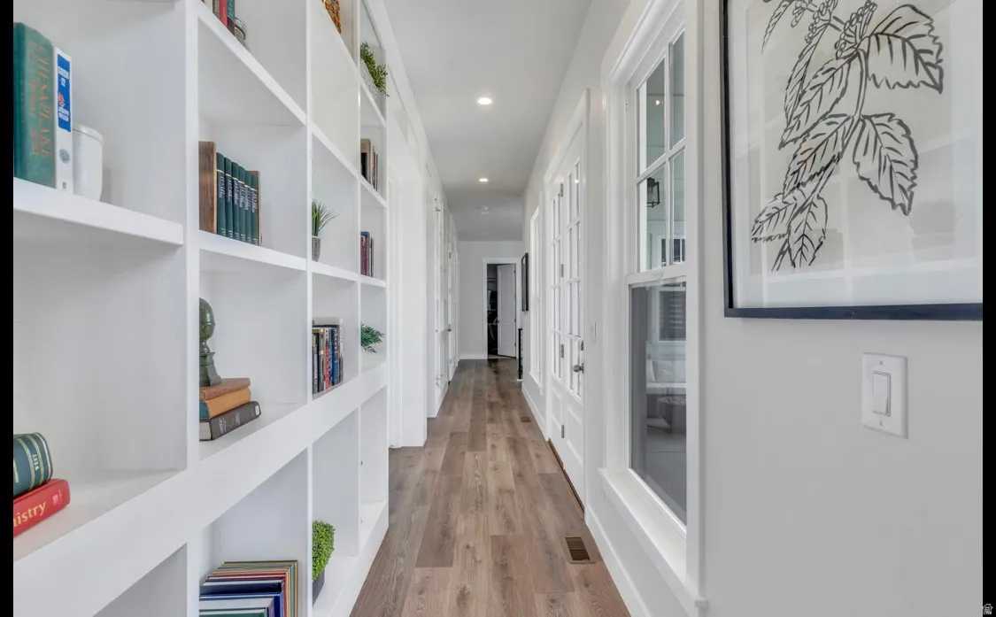 Hallway featuring extensive built-in white shelving, wood-finish flooring, recessed lighting, and multiple window openings