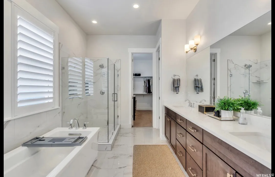 Bathroom featuring a spacious soaking tub, glass-enclosed shower, dual vanity with quartz countertop, wood-finish cabinetry, and recessed lighting