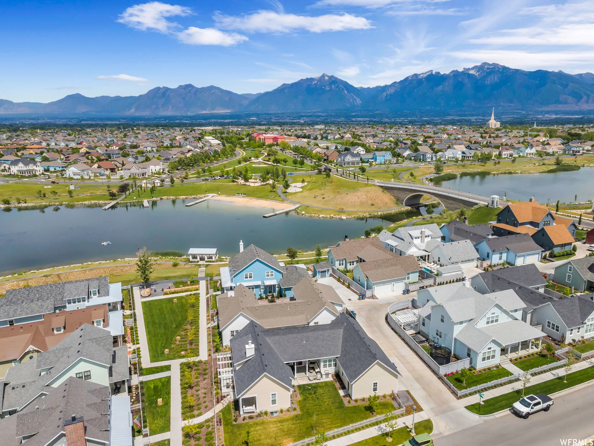 Aerial perspective showcasing a residential community situated around a body of water, featuring a sandy shoreline and a pedestrian bridge
