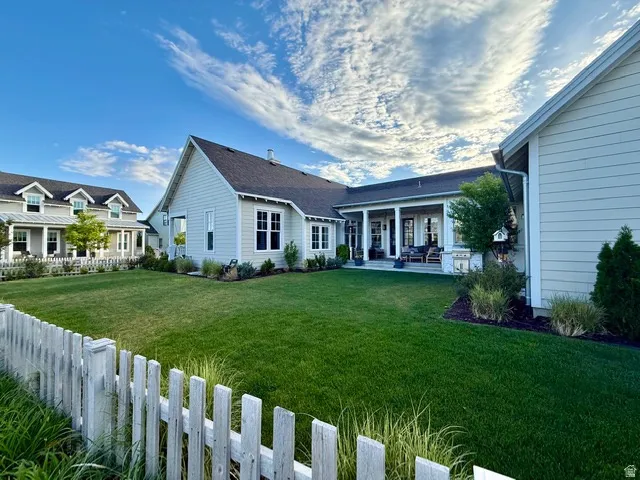 Expansive backyard featuring a manicured lawn, established landscaping, and a covered patio