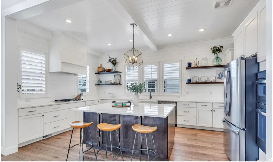 Open-concept kitchen featuring a central island with countertop seating, stainless steel appliances, white shaker cabinetry, white shiplap walls, and wood-finish flooring