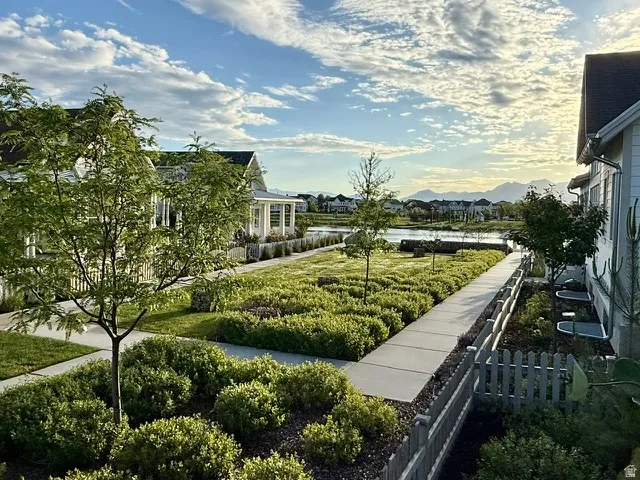 Manicured green space with mature plantings, a concrete pathway, and distant water feature