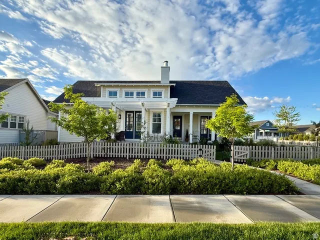 Charming cottage-style home featuring a dark shingle roof, white picket fence, and mature landscaping