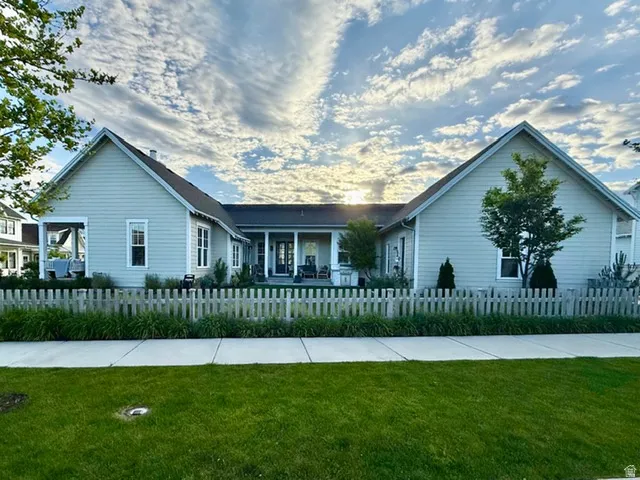Light-colored siding exterior featuring a covered porch, white picket fence, and a manicured lawn