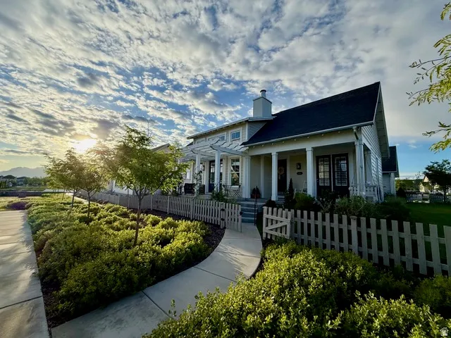 Light-colored siding exterior featuring a dark-toned roof, front porch with square columns, and a white picket fence with gate