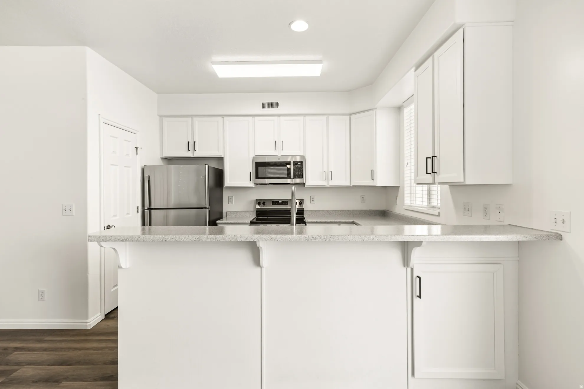 Kitchen featuring white cabinetry, stainless steel appliances, speckled countertops, and wood-finish flooring
