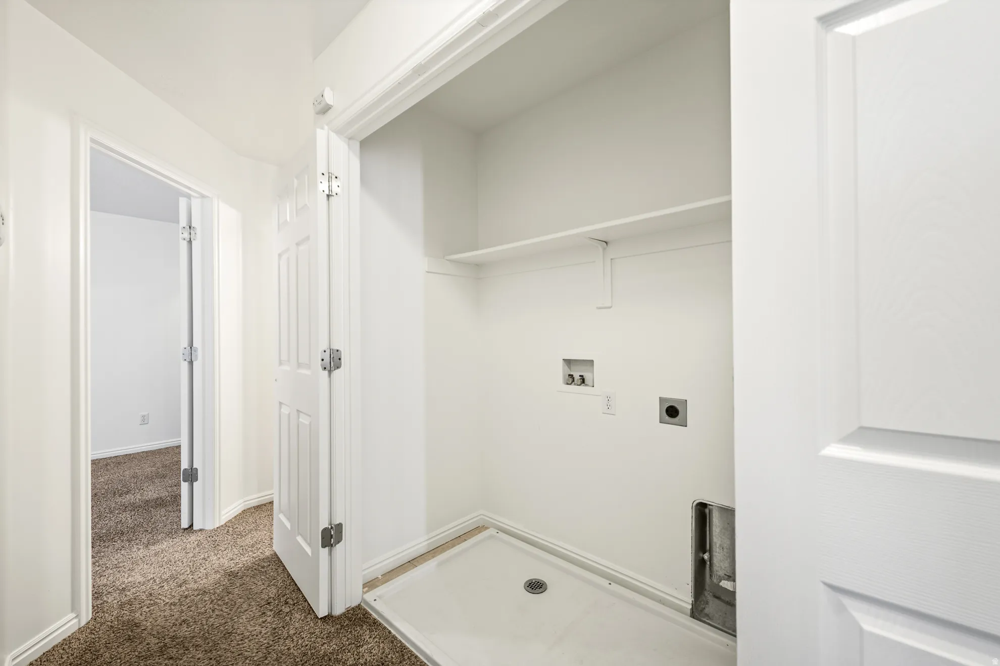Dedicated laundry area with utility hookups and a utility pan, featuring an overhead shelf and bright white walls