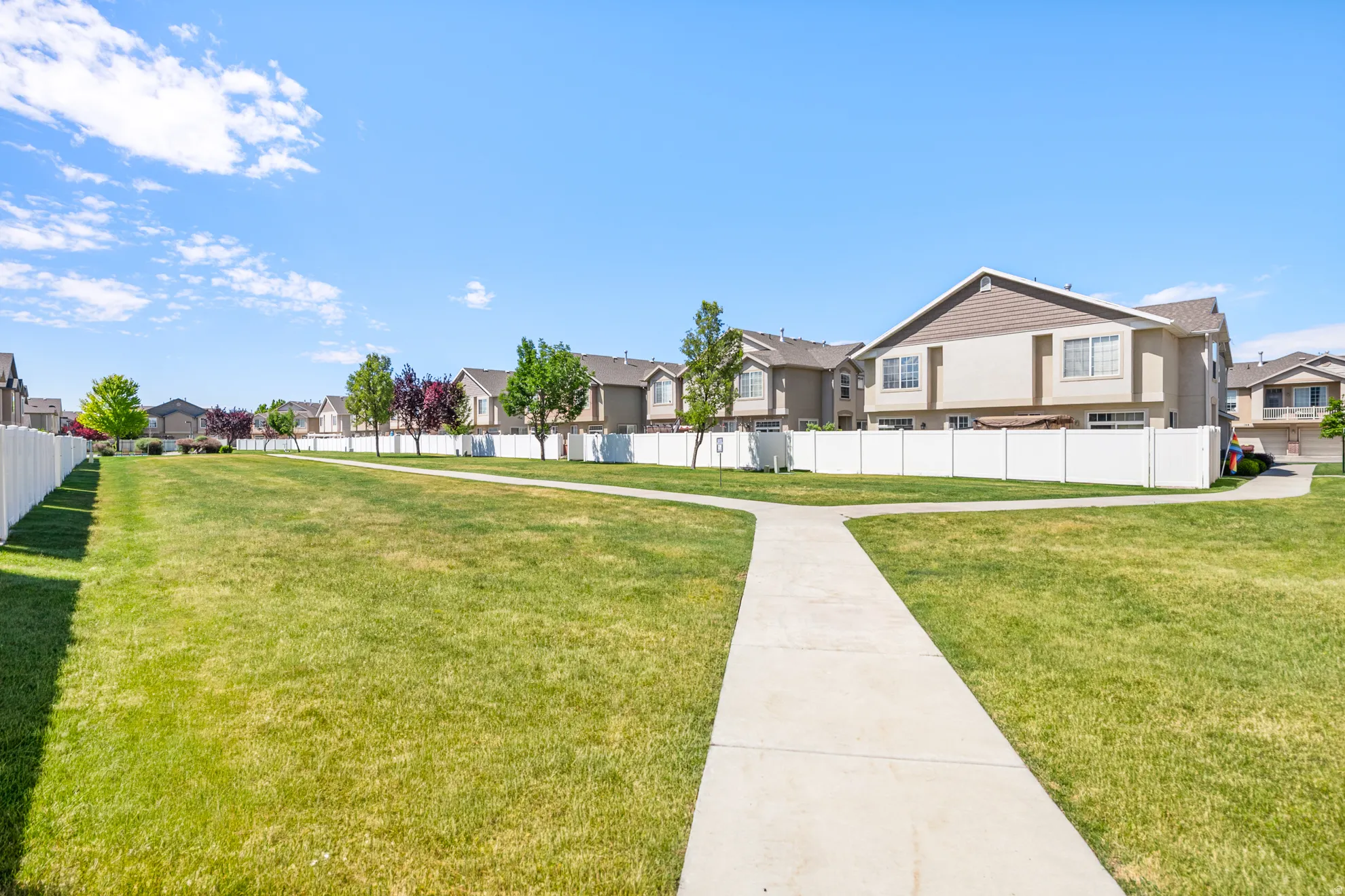 Expansive green space with a paved pathway, bordered by a white vinyl fence