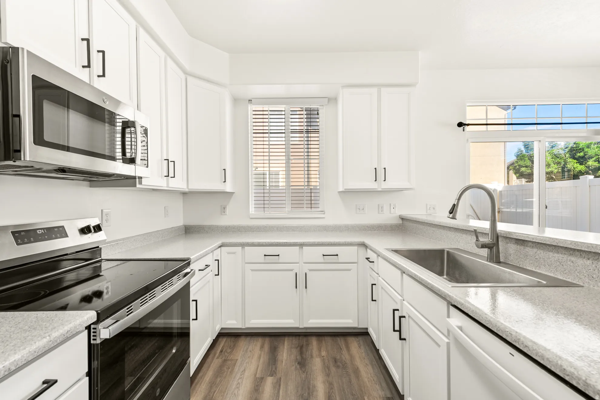 Updated kitchen featuring white shaker cabinetry, light-toned countertops, and wood-finish flooring