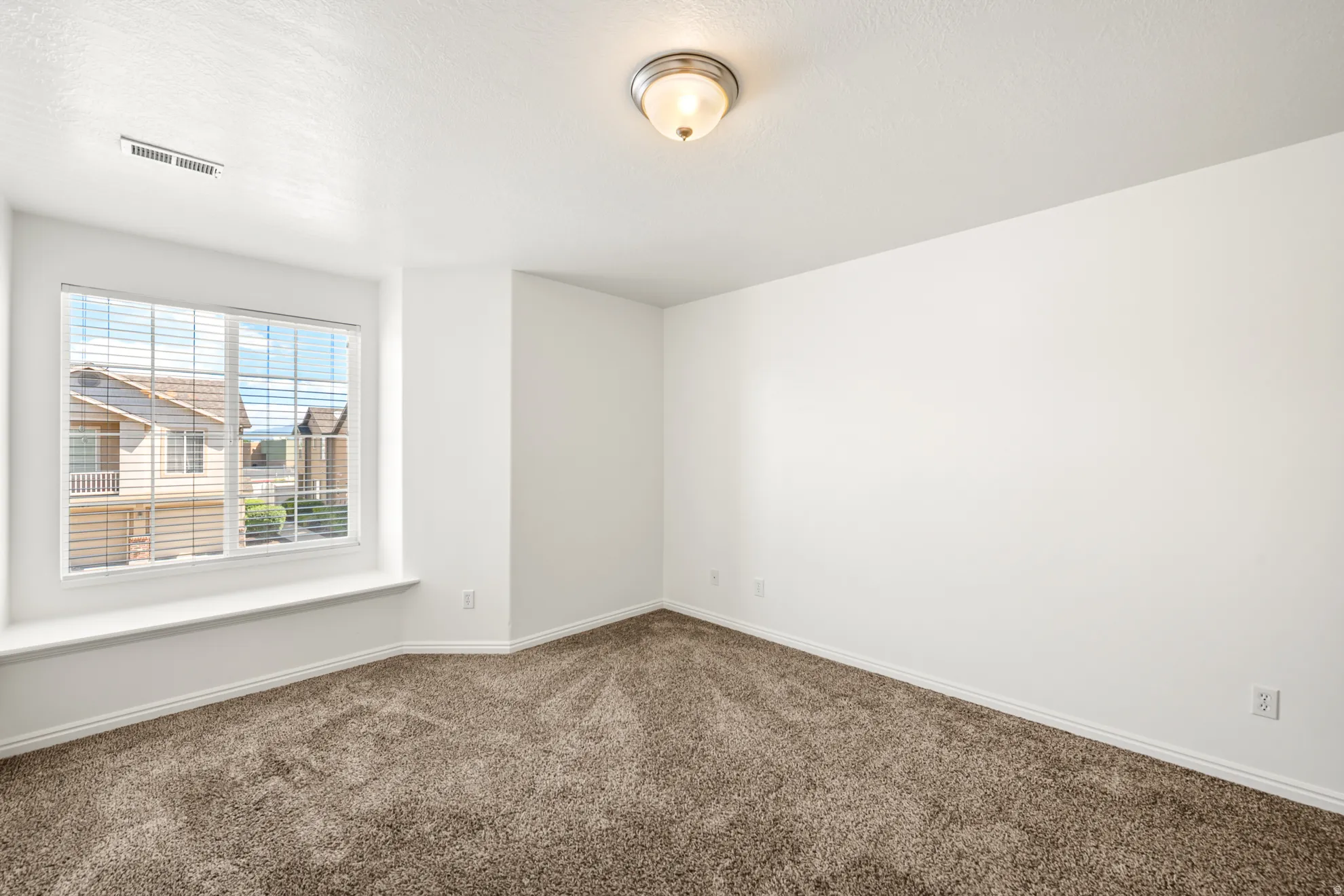 Neutral color palette throughout featuring a large window with blinds, a window seat, and plush carpet flooring