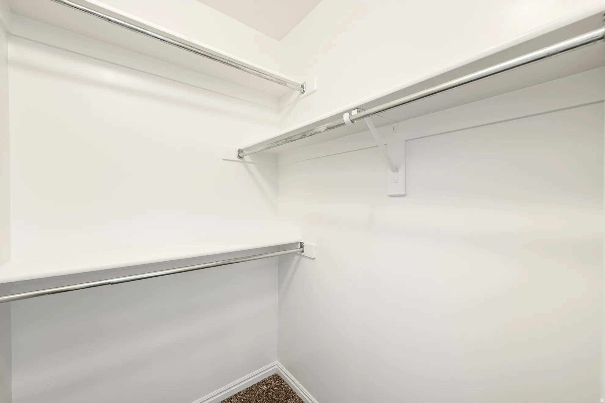 Built-in closet system featuring multiple chrome hanging rods, white shelving, and neutral carpeting