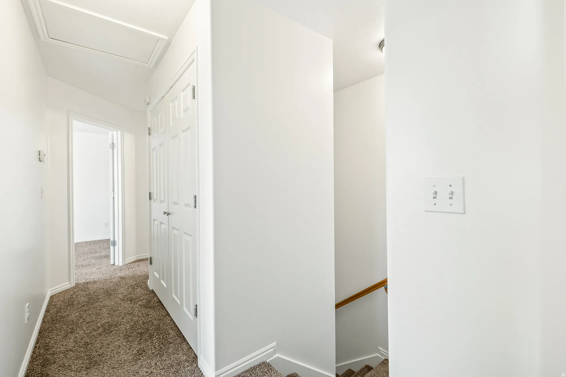 Hallway featuring white walls, textured carpeting, white trim, a closed bi-fold door, and an attic access panel
