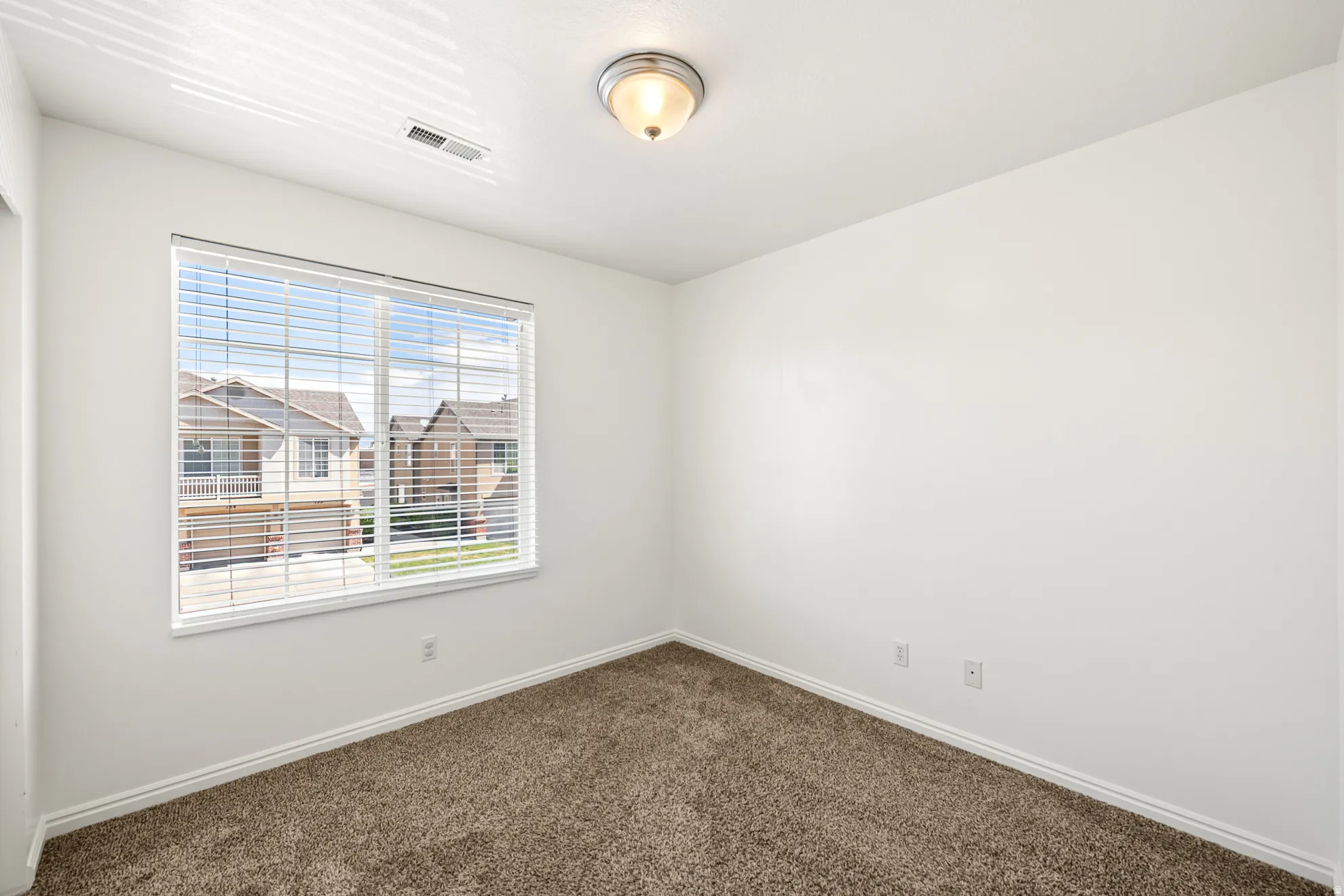 Carpeted room with a large window featuring horizontal blinds