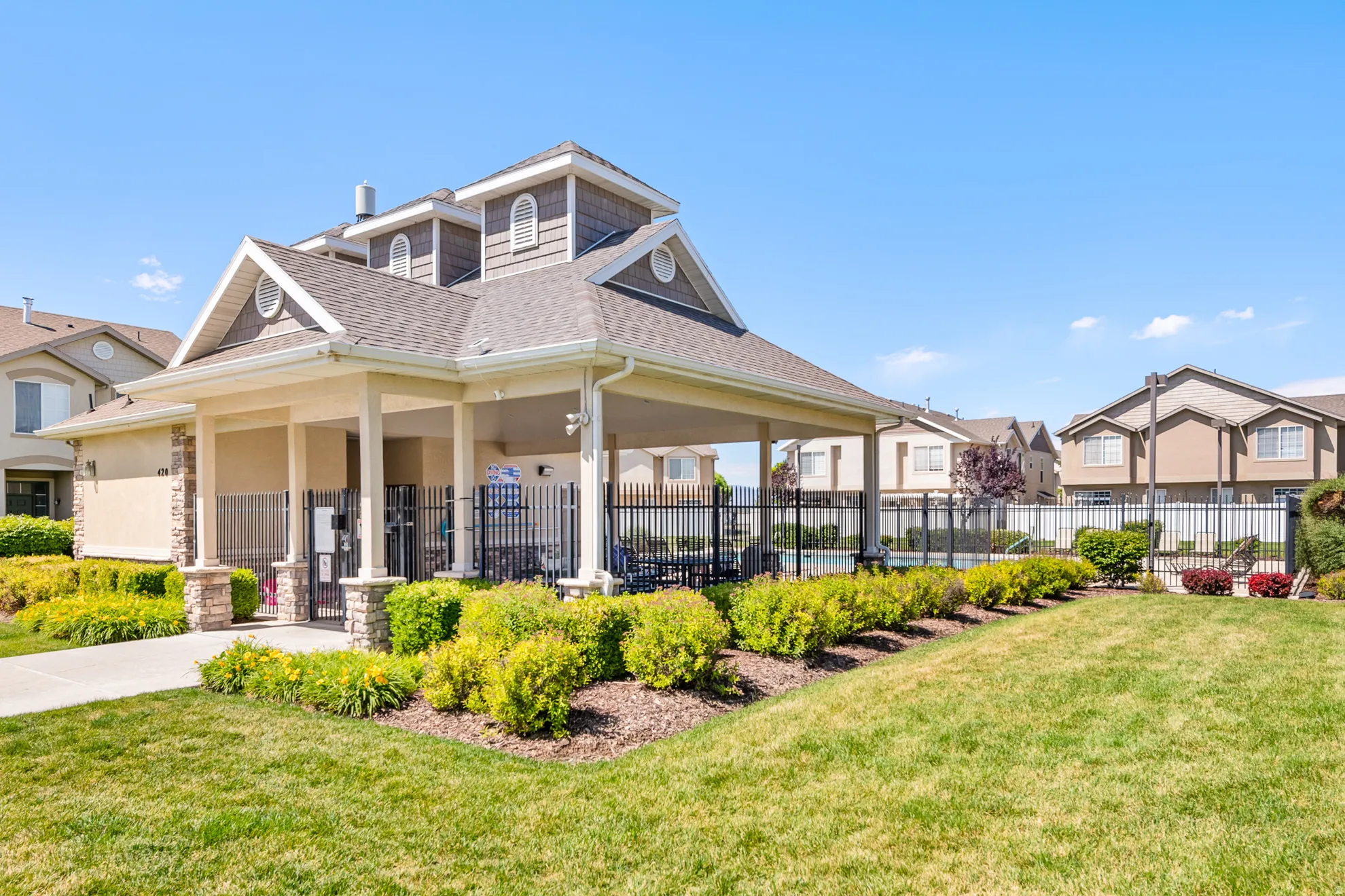 Community amenity building featuring a covered patio with stone-wrapped columns, a shingle roof, and gabled dormers