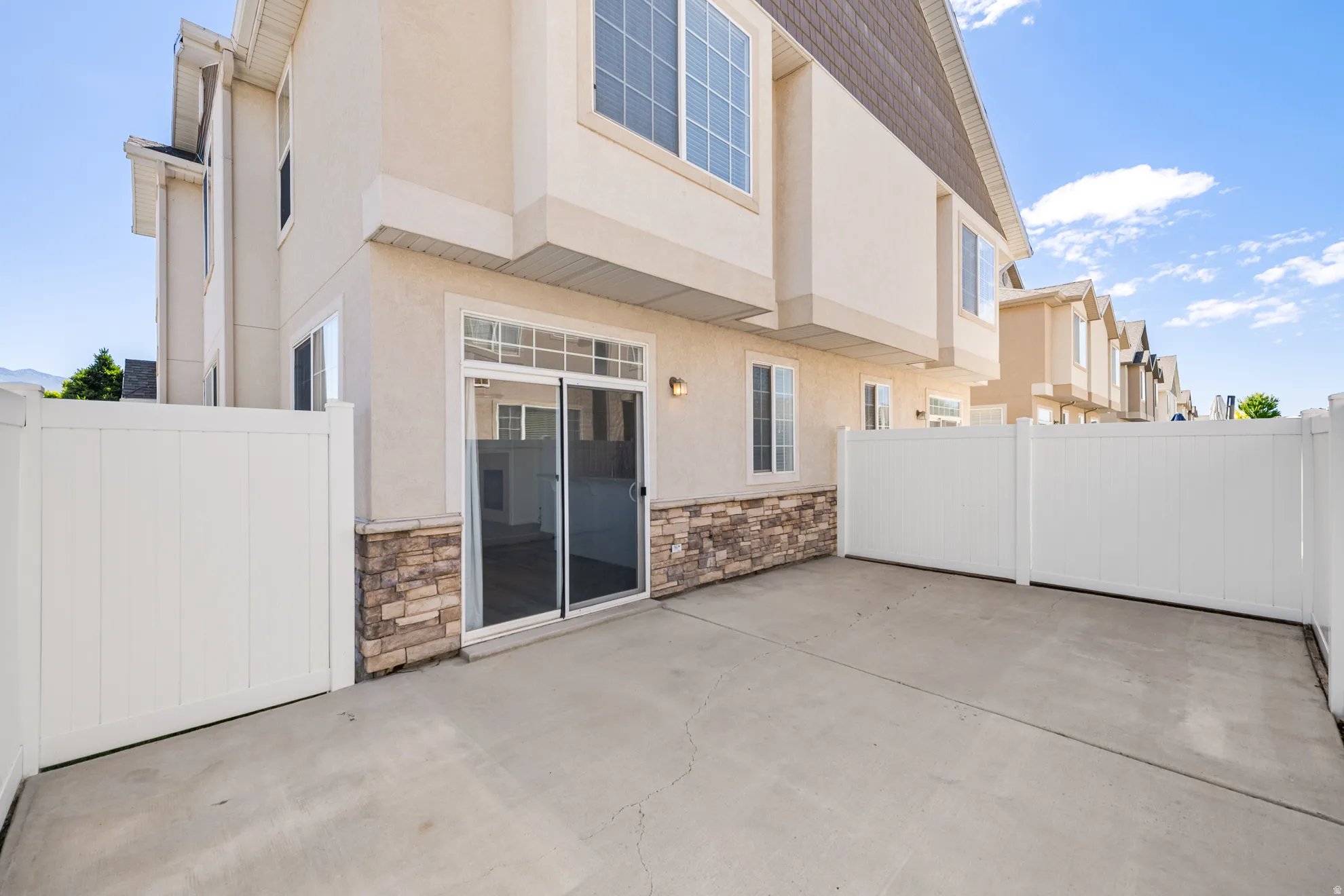 Private concrete patio surrounded by white vinyl fencing, featuring a sliding glass door entry to the interior