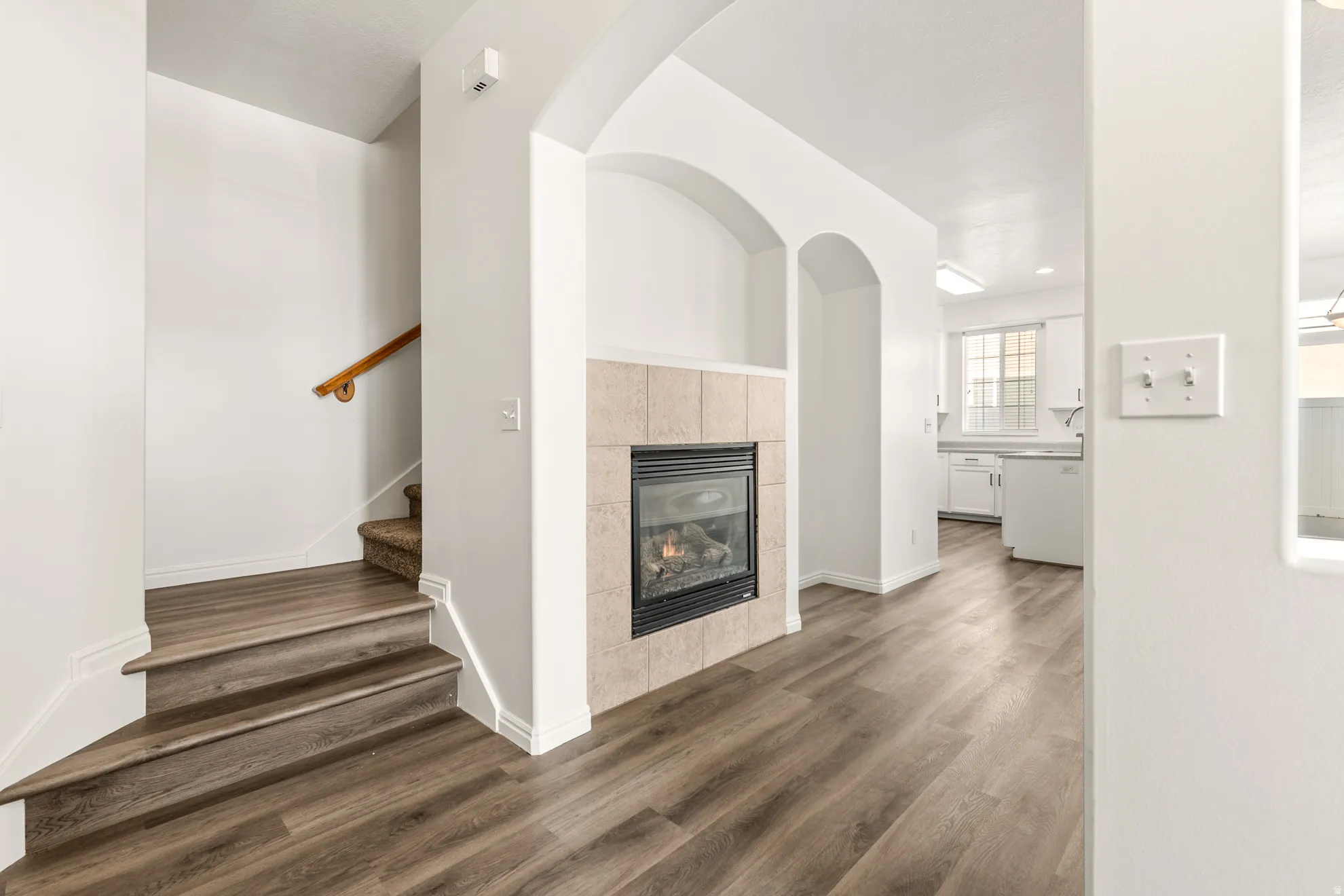 Open-concept main level featuring wood-finish flooring, a gas fireplace with tile surround, and arched architectural details
