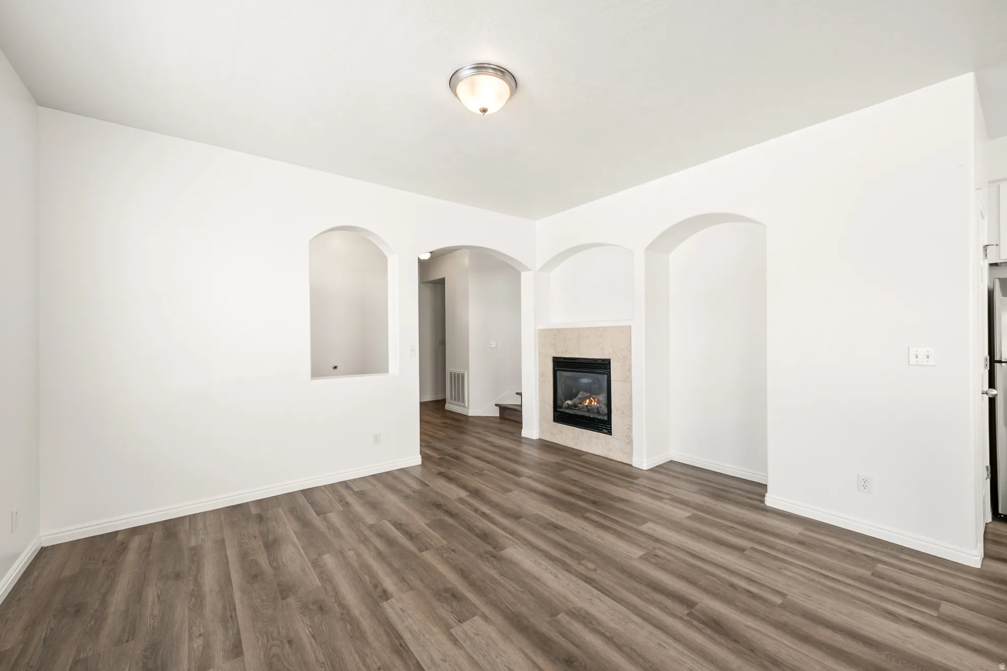 Spacious interior featuring wood-finish flooring, a contemporary fireplace with a stone surround, and arched wall niches