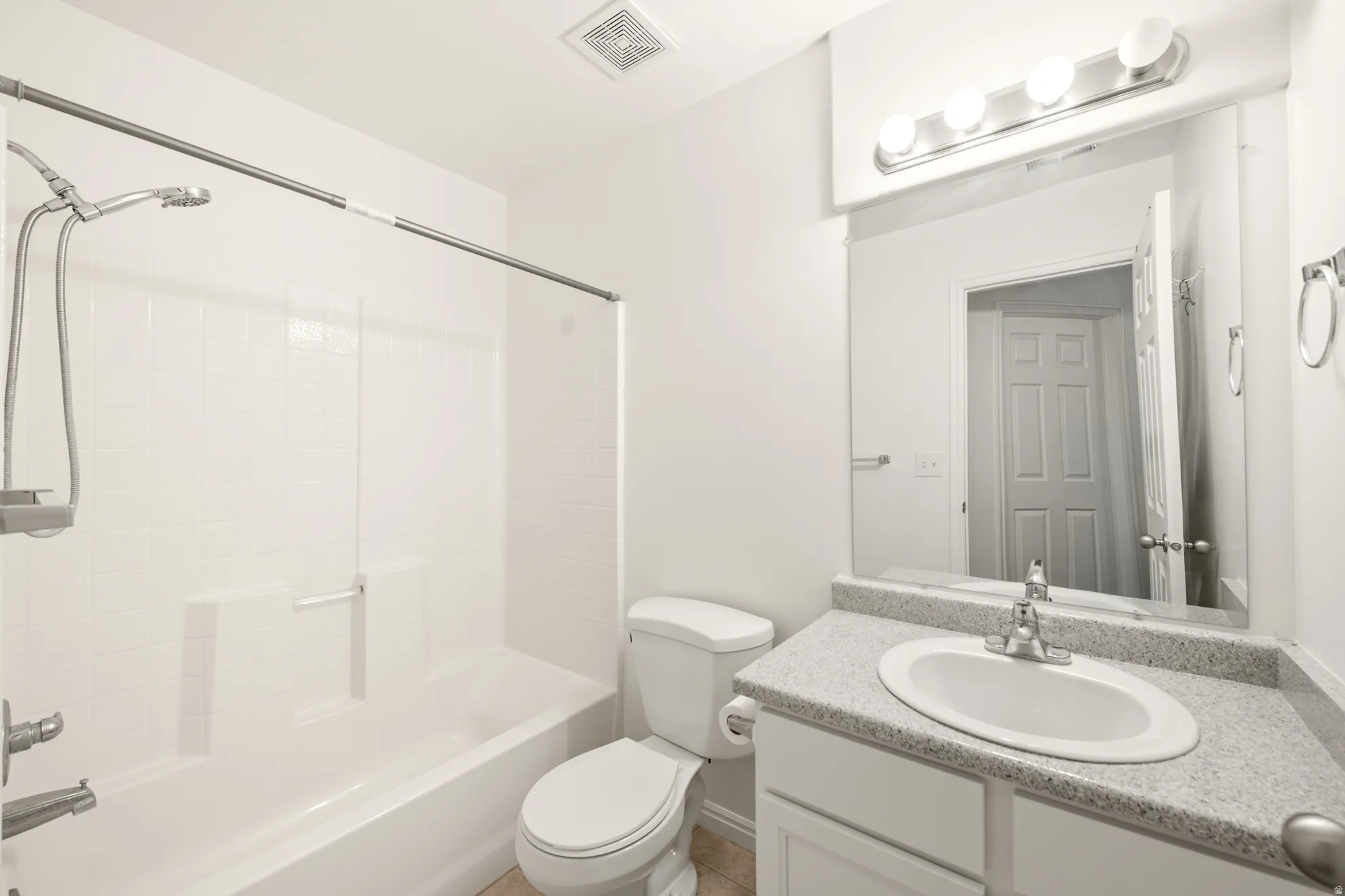 Bathroom featuring a white bathtub with a tiled surround, a white toilet, a vanity with a light-toned countertop, an oval undermount sink, and a mirrored wall cabinet with integrated lighting